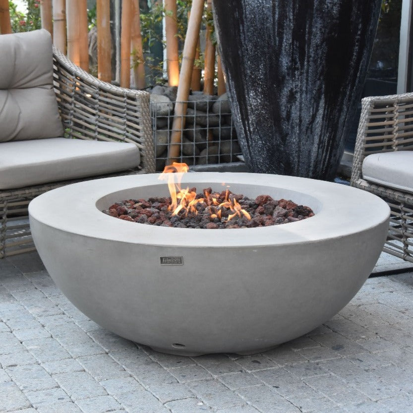 Elementi Lunar Bowl Fire Pit Table - Light Gray Lit in a garden with bamboo trees
